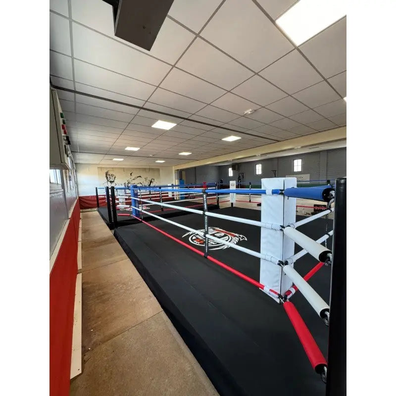 SportCom Pro-Trainingsboxring mit 30 cm Podium, in einem schmalen Raum mit Deckenleuchten, Längsansicht