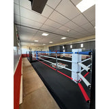 SportCom Pro-Trainingsboxring mit 30 cm Podium, in einem schmalen Raum mit Deckenleuchten, Längsansicht