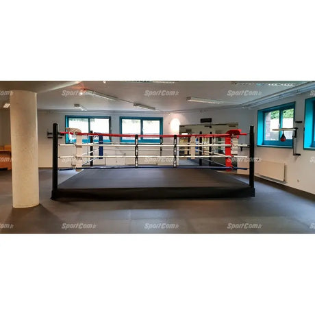 SportCom Pro-Trainingsboxring mit 30 cm Podium, in einem hellen Trainingsraum mit rot-blauen Ecken