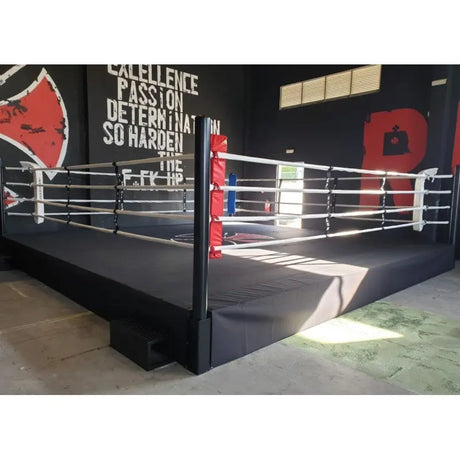 SportCom Pro-Trainingsboxring mit 50 cm Podium, in einem Gym mit Wandschriftzug, schwarzes Podium