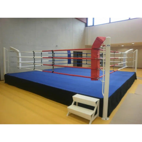 SportCom Pro-Trainingsboxring mit 50 cm Podium, mit blauem Boden und Treppe auf gelbem Hallenboden