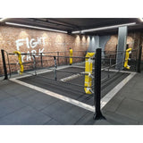 SportCom Ringplane für Bodenmontage-Boxringe – Schwarze Plane im Ring mit gelben Eckpolstern in einer Trainingshalle