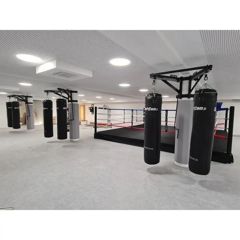 SportCom Sandsack-Wandhalterung mit Schiene und Laufwagen als freistehende Konstruktion vor dem Boxring in heller Halle