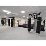 SportCom Sandsack-Wandhalterung mit Schiene und Laufwagen als freistehende Konstruktion vor dem Boxring in heller Halle