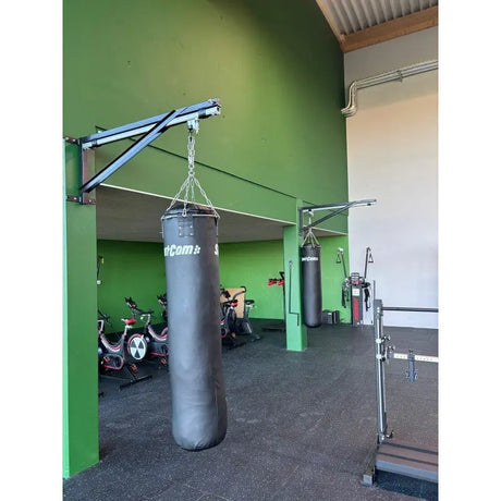 SportCom Sandsack-Wandhalterung mit Schiene und Laufwagen mit Sandsack vor grüner Wand in einer Trainingshalle