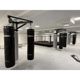 SportCom Sandsack-Wandhalterung mit Schiene und Laufwagen mit schwarzen Sandsäcken in einer Halle mit Boxring