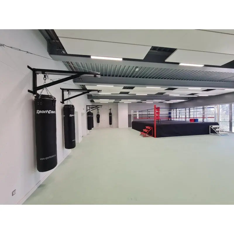 SportCom Sandsack-Wandhalterung mit Schiene und Laufwagen in einer hellen Halle mit Boxring im Hintergrund, Wandreihe