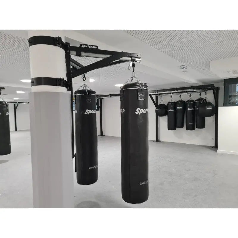 SportCom Sandsack-Wandhalterung mit Schiene und Laufwagen an einer weißen Säule mit zwei Sandsäcken in der Trainingshalle