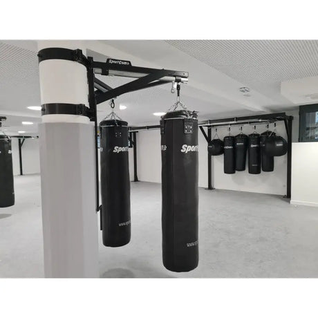 SportCom Sandsack-Wandhalterung mit Schiene und Laufwagen an einer weißen Säule mit zwei Sandsäcken in der Trainingshalle
