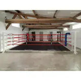 SportCom Trainings-Boxring mit 15 cm Podium, in einer Halle mit Holzbalken und roten Seilen