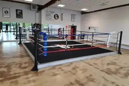SportCom Trainings-Boxring mit 15 cm Podium, in einer Halle mit Parkett und blauer Ecke