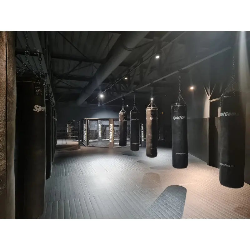 SportCom Überkopf-Förderschiene für Sandsäcke, in einem dunklen Gym mit Käfig im Hintergrund