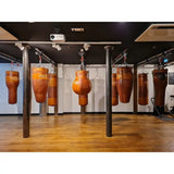SportCom Überkopf-Förderschiene für Sandsäcke, in einem Gym mit braunen Ledersäcken auf Parkett