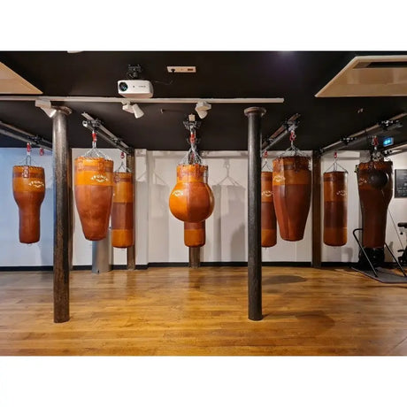 SportCom Überkopf-Förderschiene für Sandsäcke, in einem Gym mit braunen Ledersäcken auf Parkett