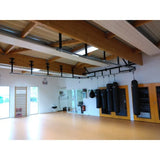 SportCom Überkopf-Förderschiene für Sandsäcke, in einer Halle mit Holzträgern und Sprossenwand