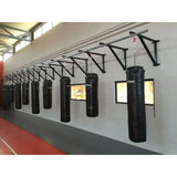 SportCom Wandmontierte Schiene für Sandsäcke, an grauer Hallenwand mit Sandsäcken und Fenstern