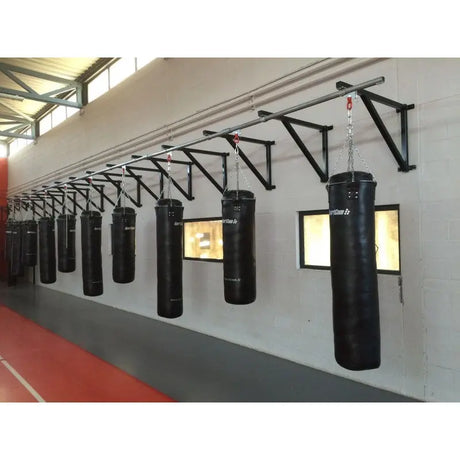 SportCom Wandmontierte Schiene für Sandsäcke, an grauer Hallenwand mit Sandsäcken und Fenstern