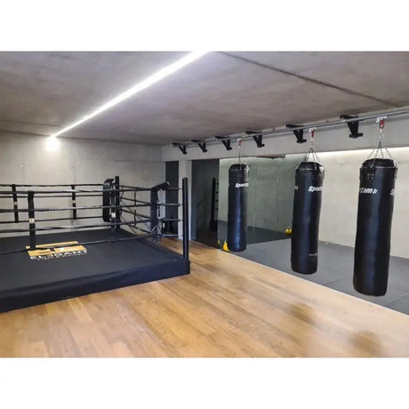 SportCom Wandmontierte Schiene für Sandsäcke, in einem Studio neben einem Boxring