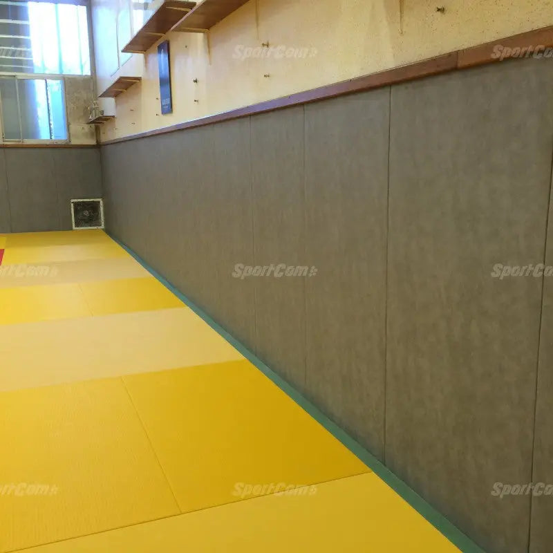 SportCom Wandpolster Standard, graue Polster entlang einer Wand über gelben Matten