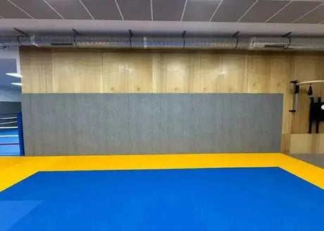 SportCom Wandpolster Standard SC-16211, graue Wandverkleidung vor Holzwand über blau-gelben Matten