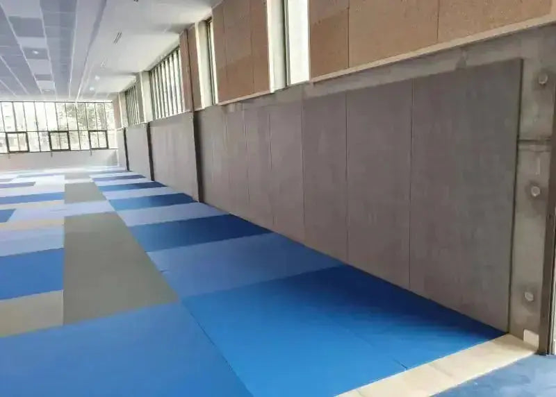 SportCom Wandpolster Standard SC-16211, lange graue Polsterreihe über blau-grauen Bodenmatten, Schrägansicht