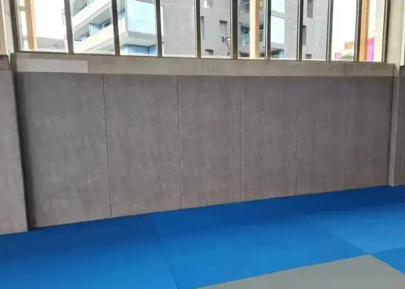SportCom Wandpolster Standard SC-16211, durchgehende graue Polsterreihe an der Wand einer Halle mit Fenstern
