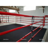 SportCom Wettkampf-Boxringseil mit Hülle, Bodenring mit roten Seilen in einem Raum mit Holzbalken