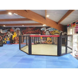 SportCom Wettkampf-MMA-Käfig 7 m auf Podium, in einem Kampfsportgym mit bunter Wandbemalung und blauen Matten