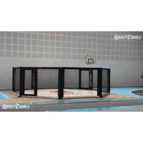 SportCom Wettkampf-MMA-Käfig 7 m auf Podium, seitlich in einer hellen Sporthalle mit Basketballkorb