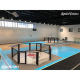 SportCom Wettkampf-MMA-Käfig 7 m auf Podium, in einer Sporthalle mit blauem Hallenboden, Blick von der Tribüne