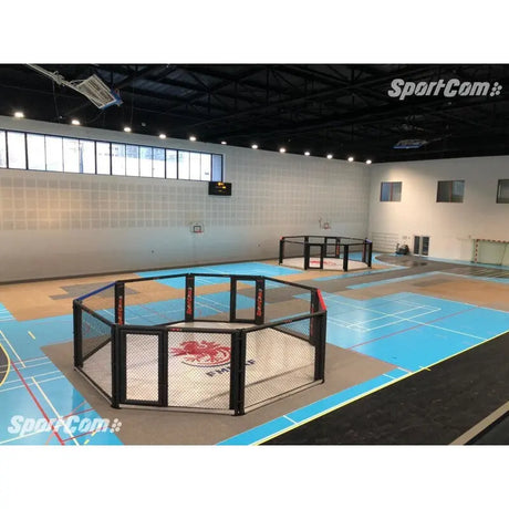 SportCom Wettkampf-MMA-Käfig 7 m auf Podium, in einer Sporthalle mit blauem Hallenboden, Blick von der Tribüne