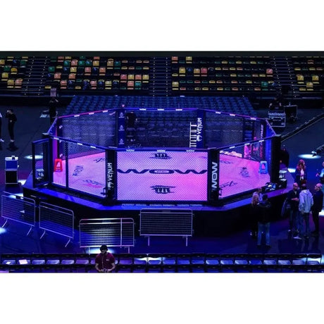 SportCom Wettkampf-MMA-Käfig Performance Oktagon, in einer Arena mit blauer Beleuchtung und vollen Tribünen