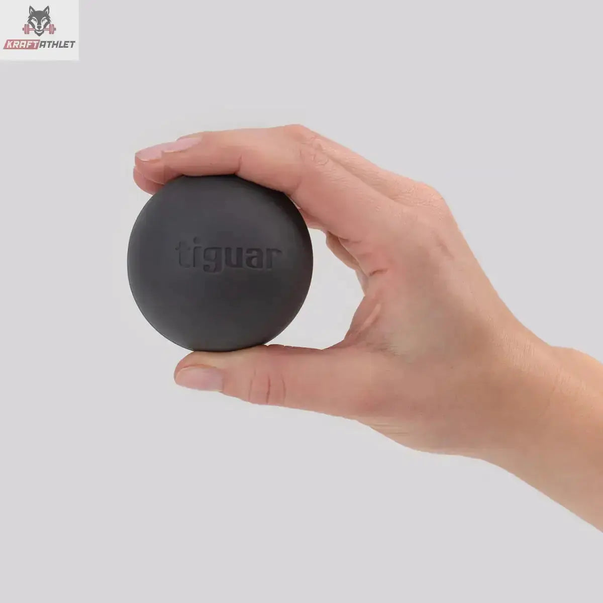 tiguar MFR Ball Massageball hart in Schwarz, Hand hält den Ball zum Größenvergleich vor grauem Hintergrund