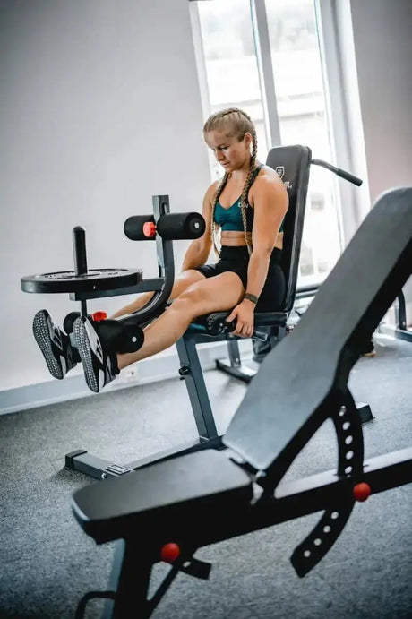 Titanium Strength 150CF Evolution Beinstrecker- und Beinbeuger-Bank: Frau sitzt auf der Bank und trainiert mit den Beinrollen, Frontansicht